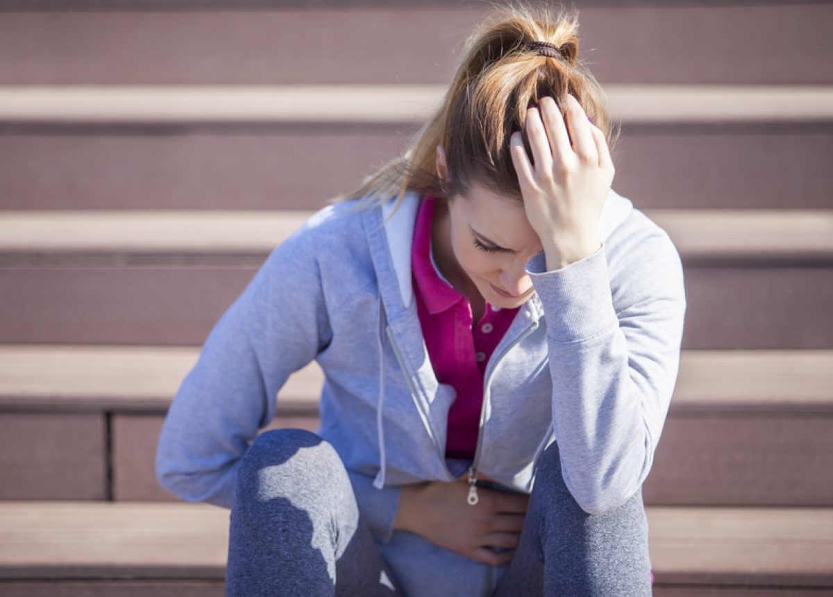 Young woman with abdominal pain after sitting on the steps of recreational running